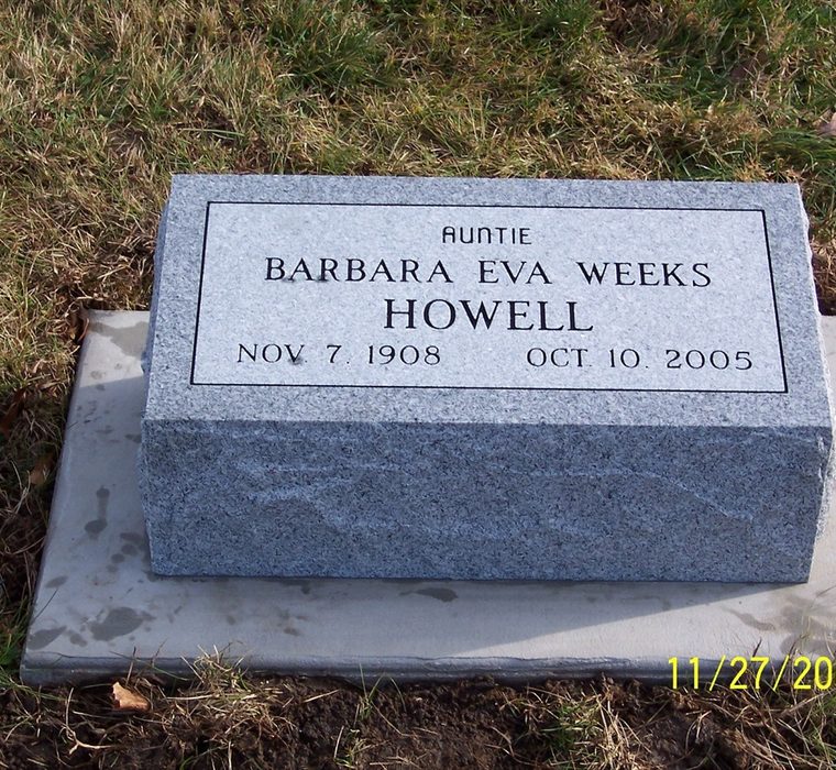Gray granite bevel marker with engraved lettering inside a bordered panel, set on a concrete pad in grass.