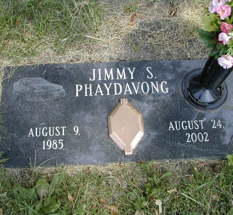 Flat black granite marker set in grass with etched car, lettering, portrait cover, and flower vase.